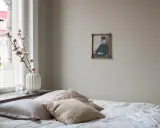 En säng med flera kuddar i olika nyanser av beige och mönster. En gammal porträttbild hänger på väggen.