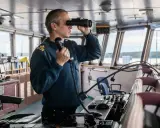 Un officier de marine, comment s'appelle la personne qui conduit un bateau, utilise des jumelles et un téléphone dans la passerelle.