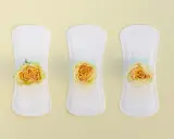 Tres compresas blancas con delicadas rosas amarillas, simbolizando un flujo escaso y la delicadeza del cuidado personal.
