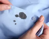 Manos sostienen camisa azul con manchas de bolígrafo. Aprende como quitar manchas de bolígrafo en ropa.