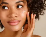 Donna con capelli ricci applica crema sul viso per una pelle bella e luminosa.