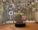 Plataforma giratoria para fotos con luces de neón "EFERVESCENCIA" y esferas blancas colgantes, creando un efecto de bullet time.