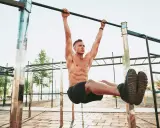 Uomo muscoloso esegue un esercizio di calisthenics per principianti alla sbarra, sollevando le gambe.