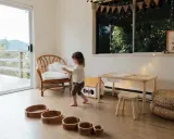 Bambina gioca in una stanza giochi in casa, tra sedie di vimini, tavolino e cesti.