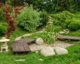 Un paisible petit jardin japonais avec des lanternes, des bancs en bois, des rochers et une végétation luxuriante.