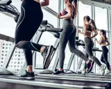 Kobiety ćwiczą cardio na bieżni, biegnąc w siłowni z widokiem na miasto.