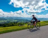 Frau fährt mit Bikepacking-Ausrüstung auf einer Straße mit Alpenpanorama.