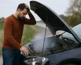 Uomo preoccupato guarda il fumo uscire dal cofano aperto, la vaschetta radiatore si svuota.