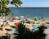 Playa de Cerdeña con niños jugando y familias disfrutando del sol bajo sombrillas coloridas.