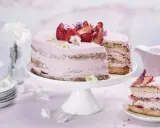 En vacker jordgubbstårta med rosa frosting och färska jordgubbar. En bit är uppskuren och ligger på en separat tallrik.
