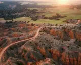 Un camino serpentea por la rambla de Barrachina, un paisaje ocre y verde bañado por el sol del atardecer.