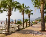 Alejka z palmami prowadzi do plaży w Marmaris, Turcja. Leżaki i parasole czekają na turystów.