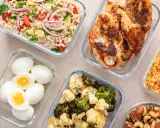 Förberedd student mat i glasbehållare: kycklingfilé, couscoussallad, grönsaker, ägg och nötter. Perfekt för en hälsosam lunchlåda.