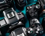 Zbliżenie na kilka nowoczesnych bezlusterkowców marek Nikon, Canon i Sony, ułożonych na turkusowym tle.