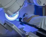 Pacjentka leży na stole terapeutycznym pod aparatem do radioterapii. Zielone linie laserowe wyznaczają pole napromieniania. To właśnie radioterapia co to jest – nowoczesna metoda leczenia.