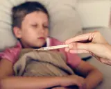 Dziecko z gorączką, czuć zimne rączki i nóżki. Mama mierzy temperaturę termometrem.