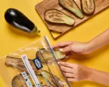 Hände legen Auberginenscheiben in einen Gefrierbeutel. So einfach ist das Aubergine einfrieren für später.