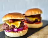 Zwei saftige Burger im Airfryer zubereitet, mit geschmolzenem Käse, knusprigem Speck und roten Zwiebeln.