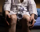 Mężczyzna w szlafroku siedzi na łóżku z budzikiem między kolanami. Czas na rozmowę o andropauzie a seksualności.