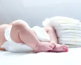 Nietolerancja laktozy u niemowlaka? Śluz w kupie może być sygnałem. Na zdjęciu nóżki dziecka i stos pieluch.