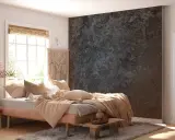 Sovrum med en säng med ljusa textilier och en dramatisk fondvägg. Väggen är målad på tapet med struktur i mörka, stenliknande toner.
