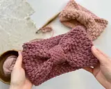 Manos sostienen una diadema tejida a crochet con un lazo. Detrás, otra diadema y ovillo de lana. ¡Descubre patrones gratis de diademas de ganchillo!