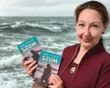 Ewa Cielesz prezentuje swoje książki "Szum" na tle wzburzonego morza.
