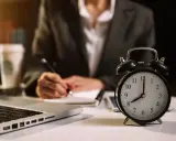 Zegar pokazuje 8:00. Zastanawiasz się, ile to godzin przy pracy na 1/2 etatu? Obok laptop, notatnik i kawa.