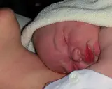 Nyfödd bebis med lite eksem på halsen, tätt intill mammas hud.