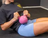 Frau macht ein **Kugelhantel Training** auf dem Boden, hält eine pinke Kettlebell und trainiert ihre Bauchmuskeln.