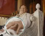 Ein Mann mit Lorbeerkranz, der an alle Kaiser Roms erinnert, sitzt auf einem Thron. Eine Lupe enthüllt Details seiner Hand.
