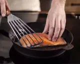 Ein Lachsfilet wird mit einem Pfannenwender in eine heiße Pfanne gelegt. Perfekt für leckere Fisch Rezepte!