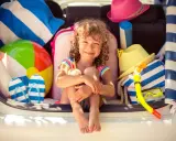 Niña sonriente rodeada de artículos de playa, lista para explorar nuevos sitios para ir con niños.