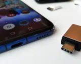 Złoty adapter USB-C i białe przejściówki leżą obok niebieskiego smartfona. Dowiedz się, jak podłączyć pendrive do telefonu.