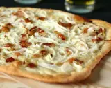 Flammekueche généreuse garnie d'oignons crus ou cuits et de lardons croustillants, prête à être dégustée.
