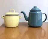 En gul gryta och en blå kaffepanna i emalj, liknande en klassisk kockums kaffepanna, står på ett träbord.