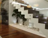 Elegante subida de escalera interior con plantas decorativas y piedras blancas.