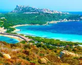 Vacker kustlinje med turkost vatten, en bro och gröna kullar. En dröm för en **Sardinien resa**.