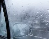 Gotas de lluvia en el cristal del coche, reflejando el exterior y el espejo retrovisor. Una escena que explica porque se empañan los cristales en días húmedos.