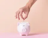 Mano inserta moneda en alcancía blanca, simbolizando cómo empezar una cuenta de ahorro.