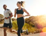 Ein Mann und eine Frau joggen lachend auf einem Feldweg. Die Sonne scheint, und die Atmung beim Joggen ist gleichmäßig und tief.