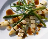 Gegrillter Spargel auf einem Teller, mit einer würzigen Sauce beträufelt und garniert mit frischen Kräutern.