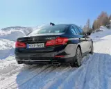 Schwarzer BMW 540i G30 fährt durch tiefen Schnee auf einer Skipiste, bergauf mit Skilift im Hintergrund.