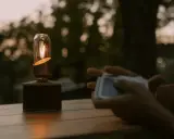 En gasollampa lyser varmt på ett träbord medan någon håller en kortlek.