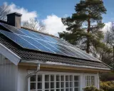 Solceller 5kw på taket av ett vitt hus, med träd och blå himmel i bakgrunden.