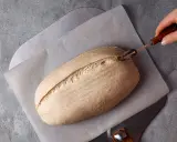 Ein Laib Brot wird mit einem Bäckermesser eingeschnitten, bereit zur Zubereitung mit Sauerteigpulver.