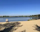 Plaża bagry z drewnianą przebieralnią i pomostem, w tle jezioro i zieleń.