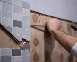 Persona usando una espátula para quitar azulejos de una pared.