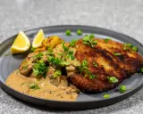 En gyllene panerad kotlett serveras med krämig svampsås, rostade potatisar, ärtor och citronklyftor.