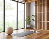 Ett ljust och luftigt yogarum hemma med stora fönster, en yogamatta, boll och en grön växt.